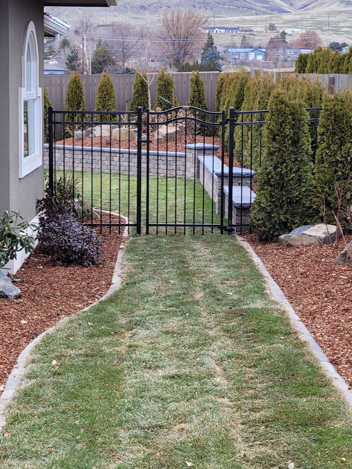 Black ornamental aluminum gate and fence framing a landscaped Yakima backyard with mountain views